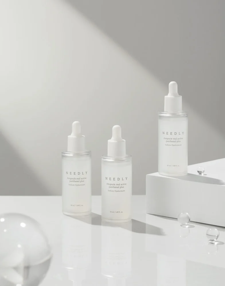 Tri bočice Divote Cosmetics seruma s kapaljkama na prozirnom stolu u minimalističkom stilu, predstavljajući proizvode korejske kozmetike.