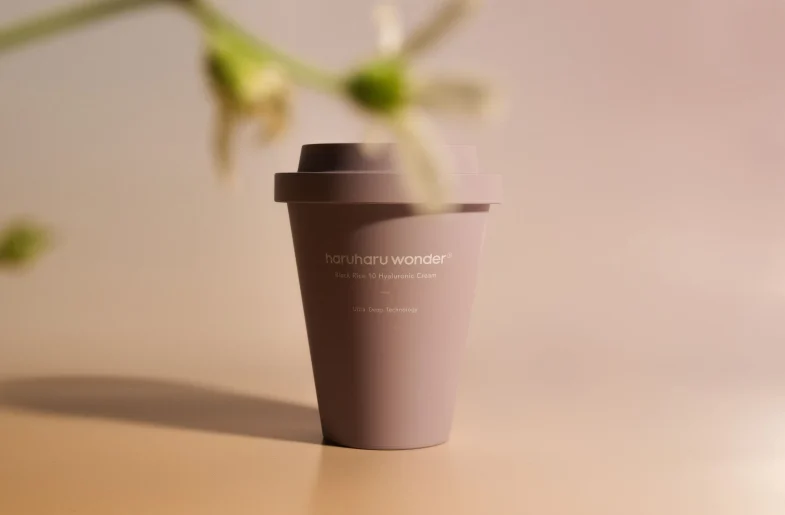 Kremasta ambalaža Haruharu Wonder, proizvoda iz linije Divote Cosmetics, simbolizira inovativnu korejsku kozmetiku, postavljena na jednostavnoj pozadini s blagim cvjetnim obrisom sprijeda.