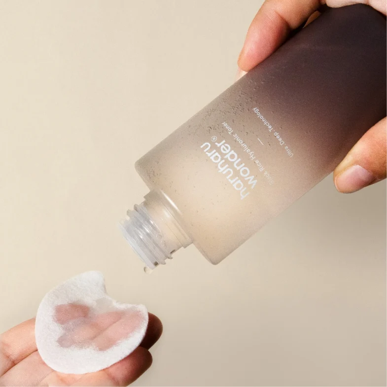 Bočica proizvoda Divote Cosmetics iz linije korejske kozmetike s tekućinom koja se nanosi na vatu, prikazana u dvije ruke na neutralnoj pozadini.