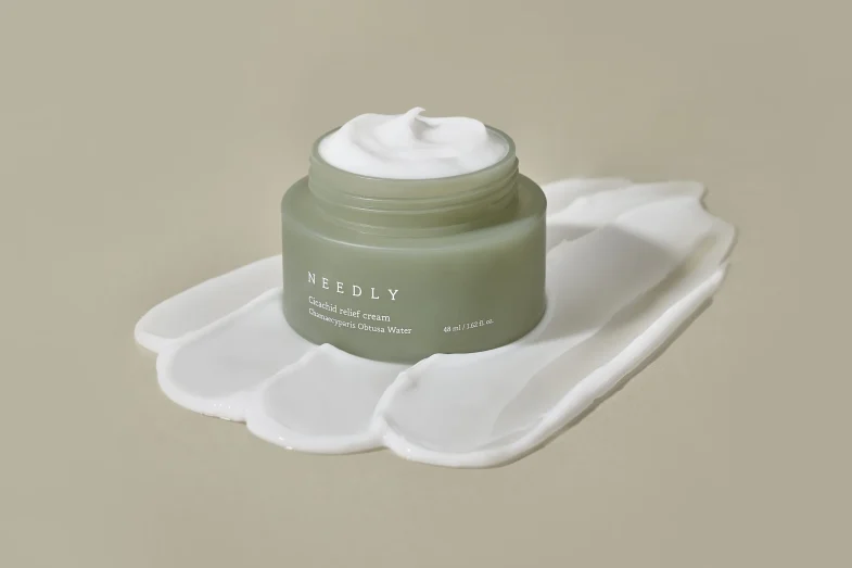 Kozmetički proizvod marke Needly, koji se često povezuje s korejskom kozmetikom, prikazan na neutralnoj pozadini, s kremom izvan posude, simbolizirajući divote cosmetics.