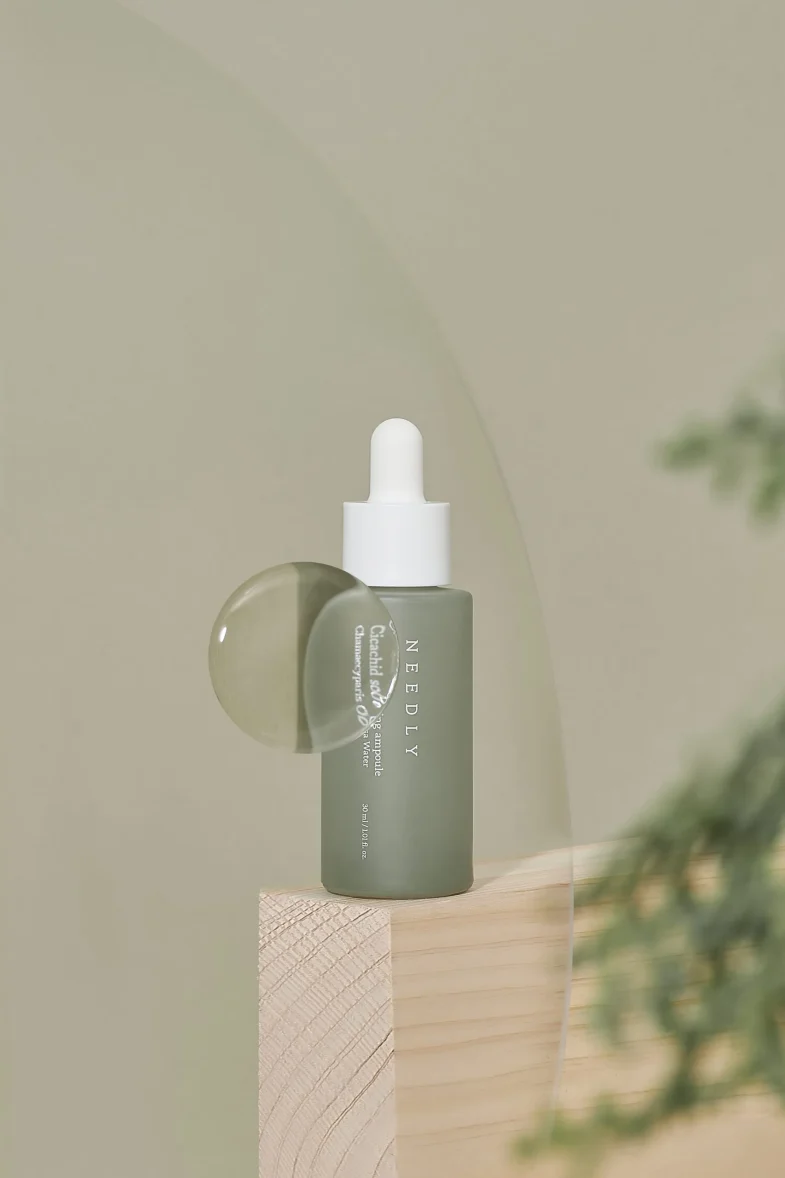 Bočica seruma 'Needly' iz kolekcije korejske kozmetike, postavljena na drvenu površinu u minimalističkom stilu, simbolizira divote cosmetics.