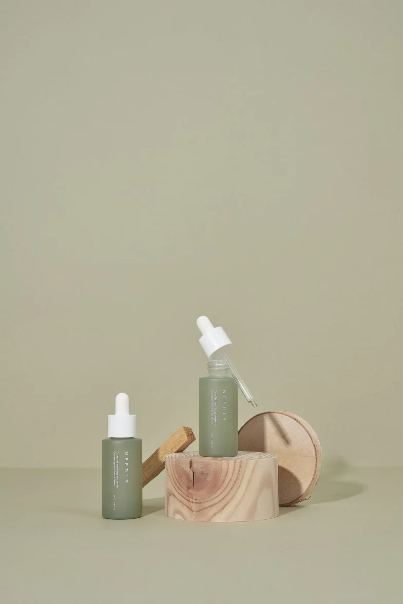Dva proizvoda Divote Cosmetics u bočicama s pipetom na drvenim postoljima, prikazuju minimalistički dizajn korejske kozmetike u neutralnoj boji.