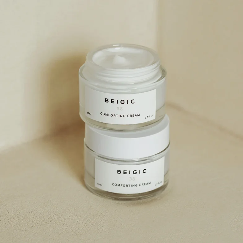 Dva staklena spremnika s bijelom kremom, označeni kao Beigic Comforting Cream, koja je popularna u divote cosmetics i korejskoj kozmetici, postavljeni su jedan na drugog na neutralnoj pozadini.