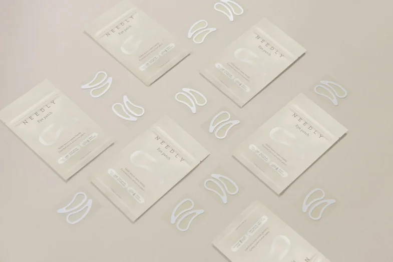 Paketići korejske kozmetike "Divote Cosmetics" s eye patch maskama ravnomjerno su raspoređeni na neutralnoj pozadini.