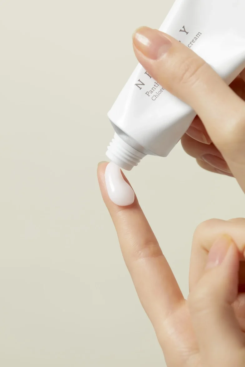 Osoba nanosi kremu Divote Cosmetics, reprezentativnu za korejsku kozmetiku, na vrh prsta iz bijele tube na bež pozadini.