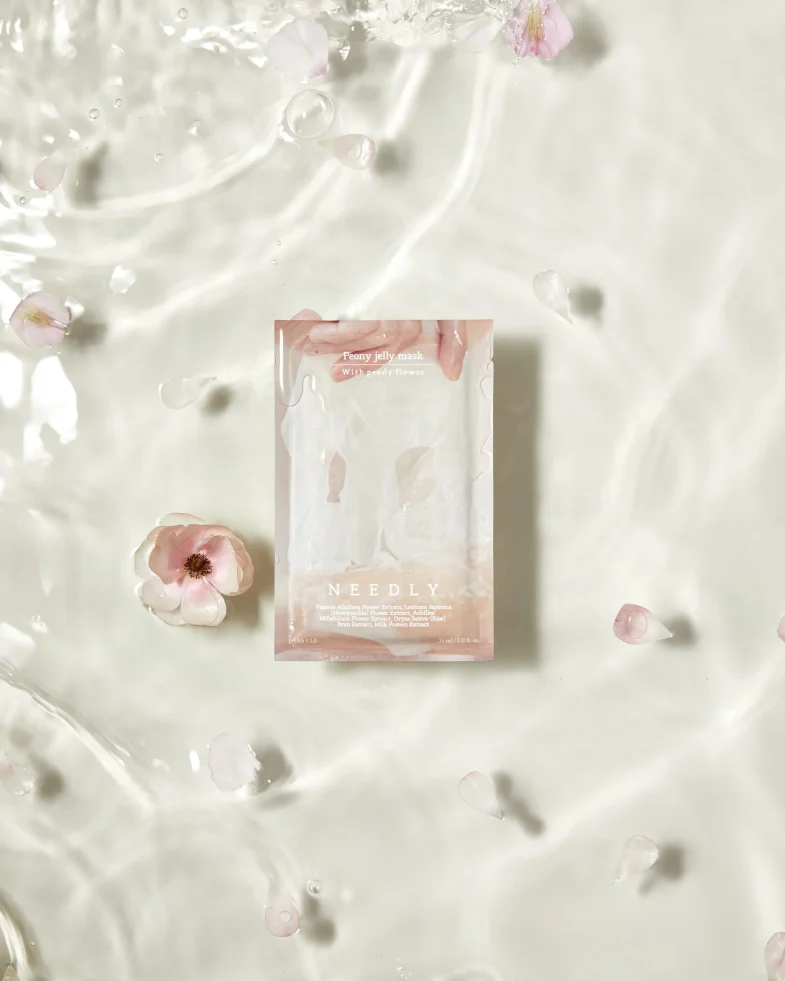 Pakiranje maske Peony Jelly od Divote Cosmetics, dio korejske kozmetike, okruženo bijelim cvjetovima na svijetloj vodenoj površini.