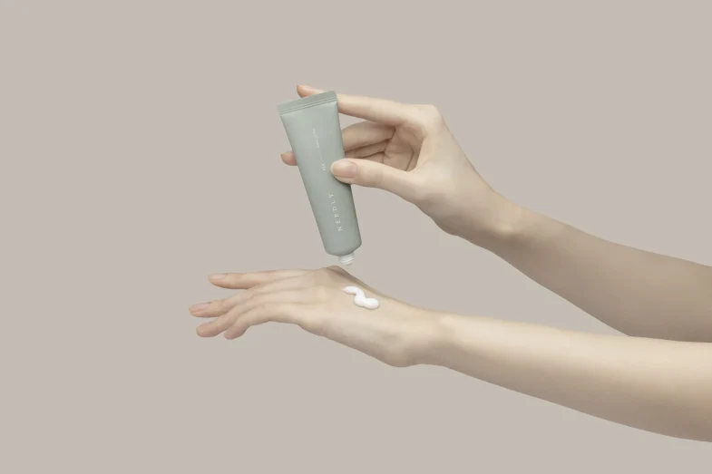 Ruke nanose kremu iz tube s oznakom 'NEEDLY', primjer korejske kozmetike iz kolekcije Divote Cosmetics.