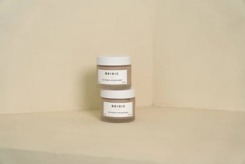 Dva staklena posudica s bijelim poklopcima i etiketom na kojoj piše 'BEIGIC 42 Softening Infused Mask', predstavljaju proizvod korejske kozmetike marke Beigic, pogodne za 'divote cosmetics'.