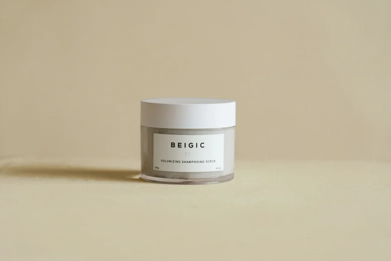 Staklena posuda s bijelim poklopcem na bež pozadini, s oznakom "BEIGIC 31 Volumizing Shampooing Scrub", koja predstavlja luksuz korejske kozmetike i divote cosmetics.