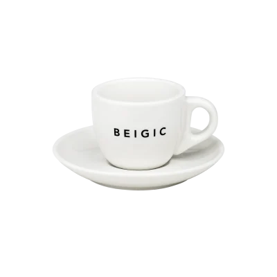 Šalica s tanjurićem s natpisom 'BEIGIC', povezana s brendom Divote Cosmetics i korejskom kozmetikom, na bijeloj pozadini.