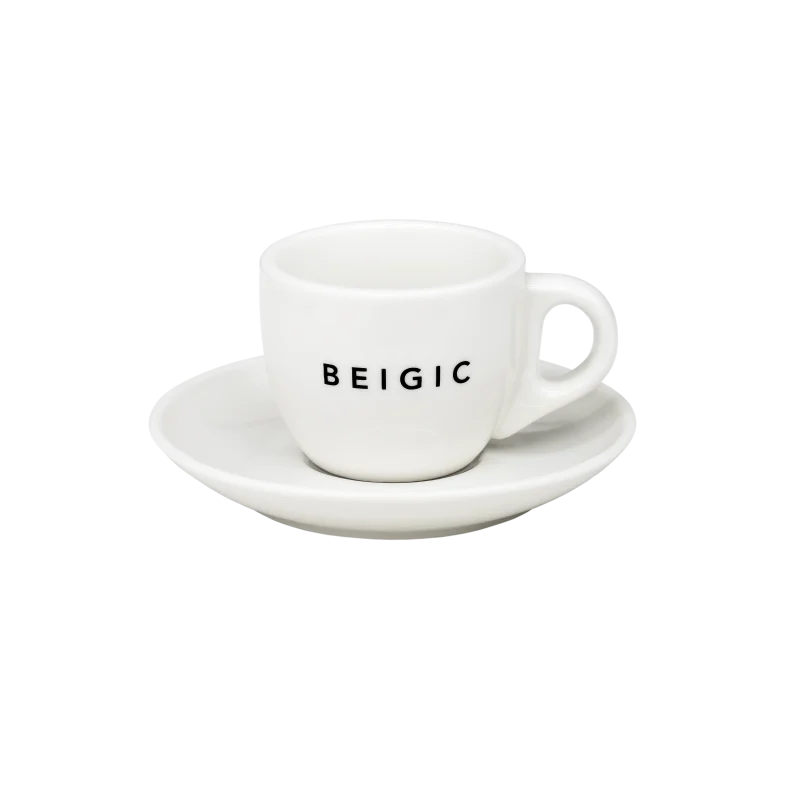 Šalica s tanjurićem s natpisom 'BEIGIC', povezana s brendom Divote Cosmetics i korejskom kozmetikom, na bijeloj pozadini.