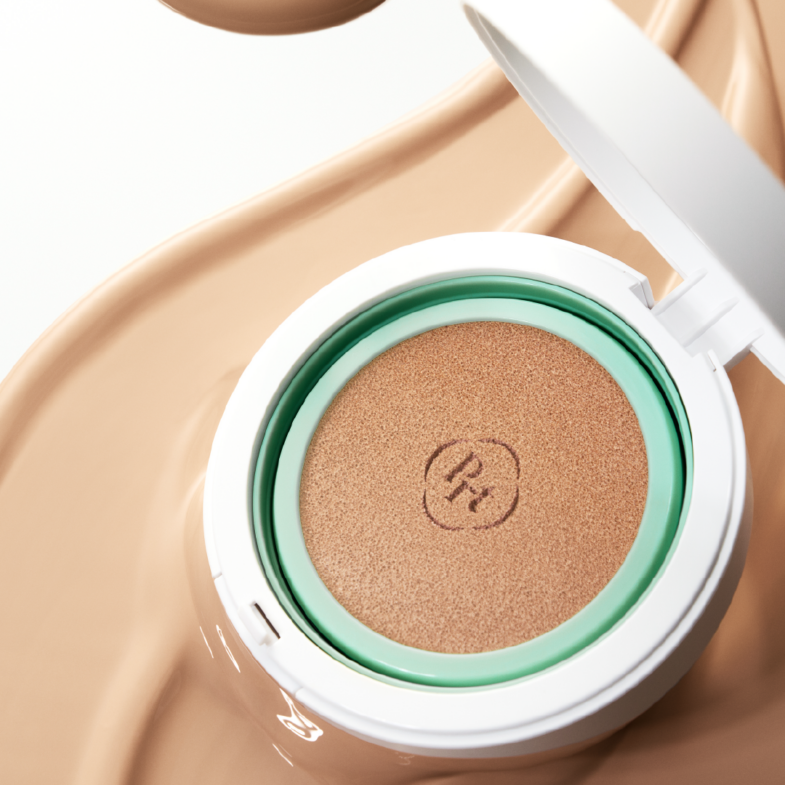 Kompaktni puder Divote Cosmetics inspiriran korejskom kozmetikom, s bijelim kućištem i smeđim puderom unutar njega, na pozadini boje kože.