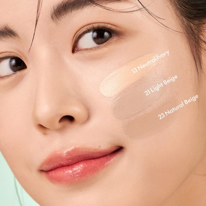 Žena s tri nijanse pudera Divote Cosmetics nanesenih na obraz, tonaliteti označeni kao '13 Neutral Ivory', '21 Light Beige' i '23 Natural Beige', što ističe raznolikost korejske kozmetike.