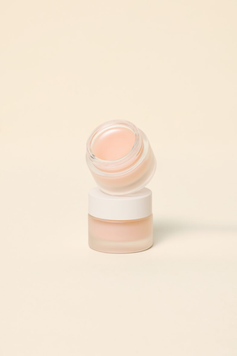 Dva staklena kozmetička pakiranja s bijelim poklopcima, jedno složeno na drugo, na neutralnoj pozadini, predstavljaju proizvode 'Divote Cosmetics' iz kolekcije korejske kozmetike.