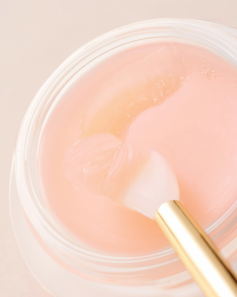 Ružičasta krema iz kolekcije korejske kozmetike Divote Cosmetics u staklenoj posudi, s aplikatorom u zlatnoj boji.