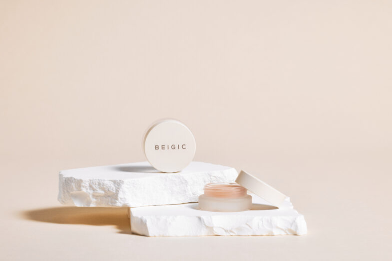 Elegantan prikaz proizvoda korejske kozmetike "Divote Cosmetics", krema marke BEIGIC postavljena na teksturiranoj bijeloj podlozi u minimalističkom okruženju u boji pijeska.