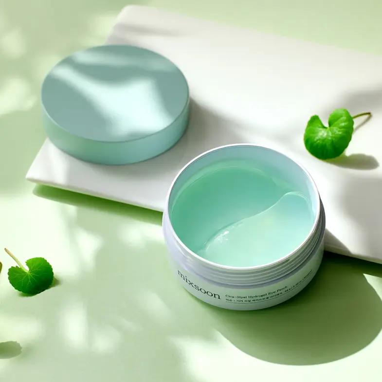 Posuda s korejskom kozmetikom "Divote Cosmetics" Hydrogel Eye Patch, otvorena na zelenoj pozadini s nekoliko zelenih listova.