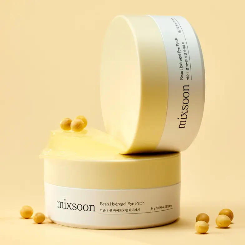 Proizvod Mixsoon Bean Hydrogel Eye Patch, koji pripada kategoriji korejske kozmetike, s posudama krem boje postavljenim na bež pozadini i zrna graha oko pakiranja, povezan s brendom Divote Cosmetics.
