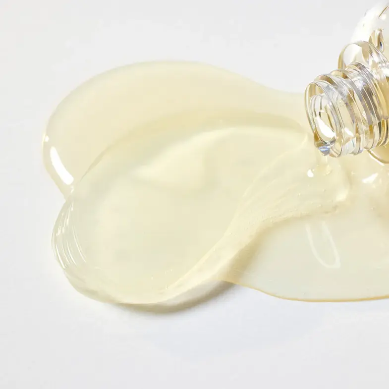 Prozirna bočica s tekućom tvari koja se izlijeva na bijelu površinu, simbolizirajući korejsku kozmetiku, povezanu s brandom Divote Cosmetics.