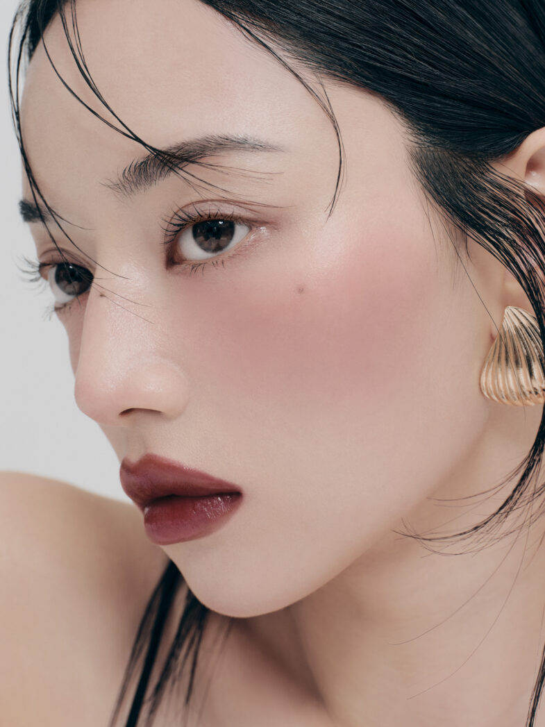 Žena s elegantnom šminkom i glamuroznim naušnicama, prikazujući korejsku kozmetiku brenda Divote Cosmetics.