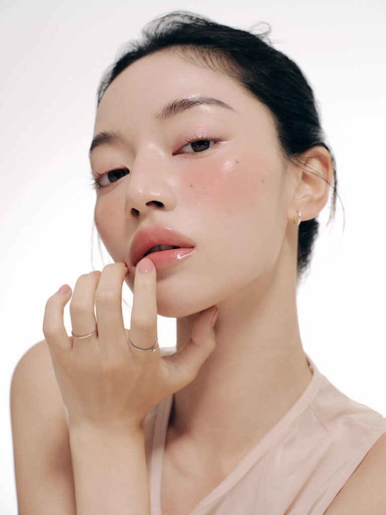 Žena s elegantnim minimalističkim makeupom koji ističe sjajnu i zdravu kožu, naglašavajući korejsku kozmetiku i efekt Divote Cosmetics proizvoda.