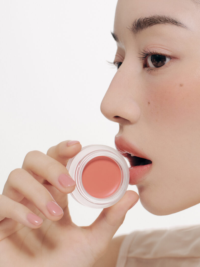 Profil žene koja drži posudicu s ružičastim rumenilom marke Divote Cosmetics, što predstavlja proizvod iz korejske kozmetike.