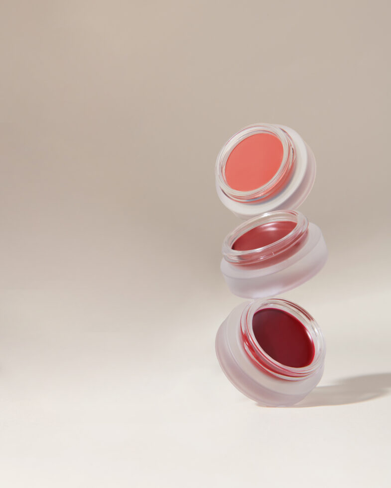 Tri lebdeće bočice korejskog ruža u različitim nijansama, primjer korejske kozmetike marke Divote Cosmetics, na neutralnoj pozadini.